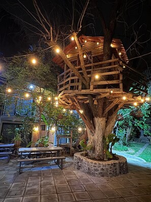 A treehouse structure with a wooden platform and a stone base, surrounded by string lights and potted plants. - Hotel Casa Grangelo (Atlixco)