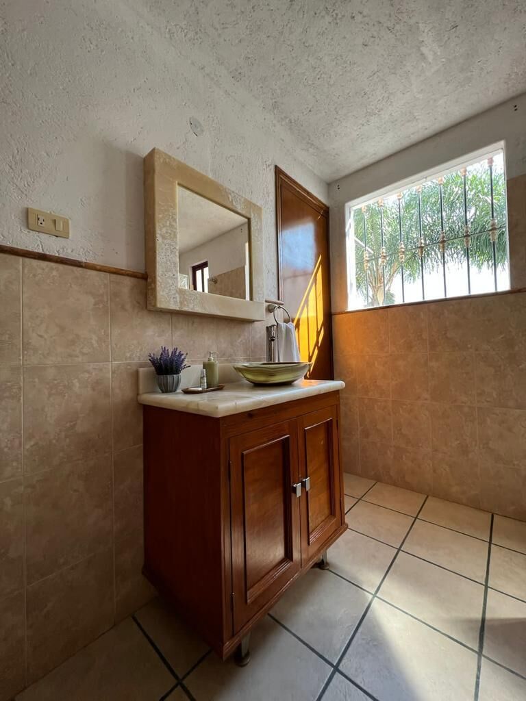 Un baño con un mueble de madera, un espejo y una ventana con vista a follaje.
