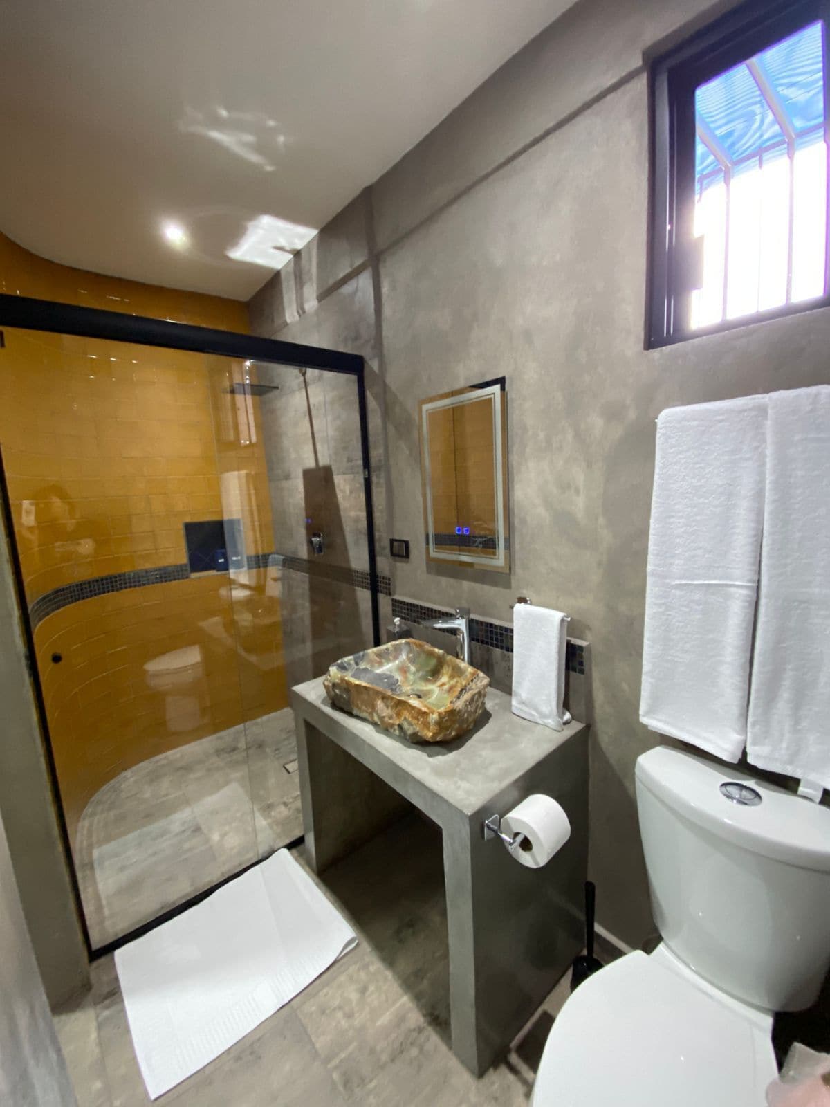Un baño moderno con cabina de ducha de vidrio, lavamanos de mármol, inodoro y toallero.