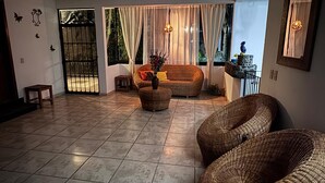 A spacious living area with a tiled floor, wicker furniture, and a view through a large window. - Hotel Casa Grangelo (Atlixco)