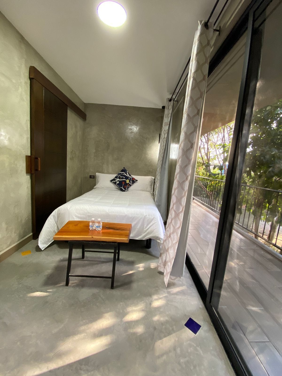 A bedroom with a bed, a wooden table, a window with a view, and a door.