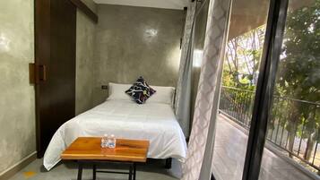 A bedroom with a bed, a wooden table, a window with a view, and a door.