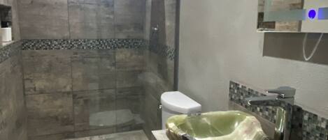 Ein Badezimmer mit Toilette, einem Waschbecken mit ungewöhnlicher Formgebung und einer Duschkabine.