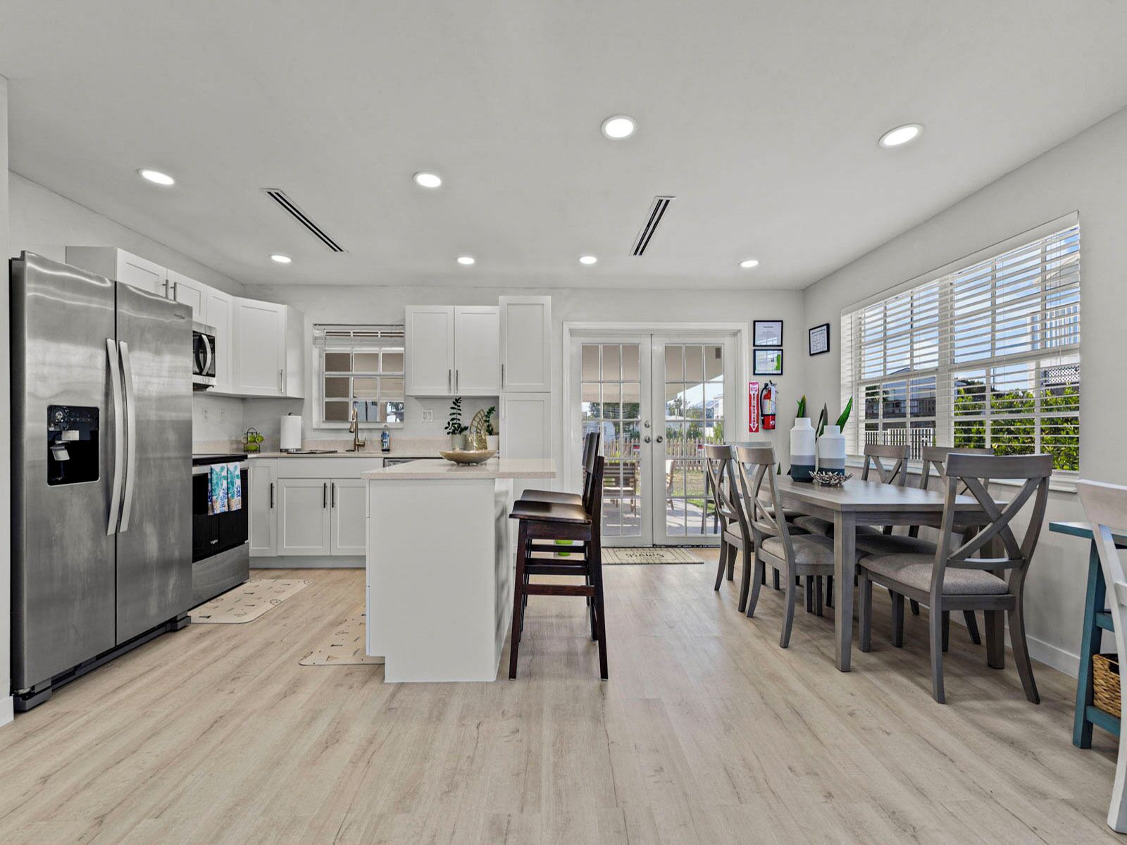 A modern kitchen with white cabinetry, a stainless steel refrigerator, and a dining area with a table and chairs.