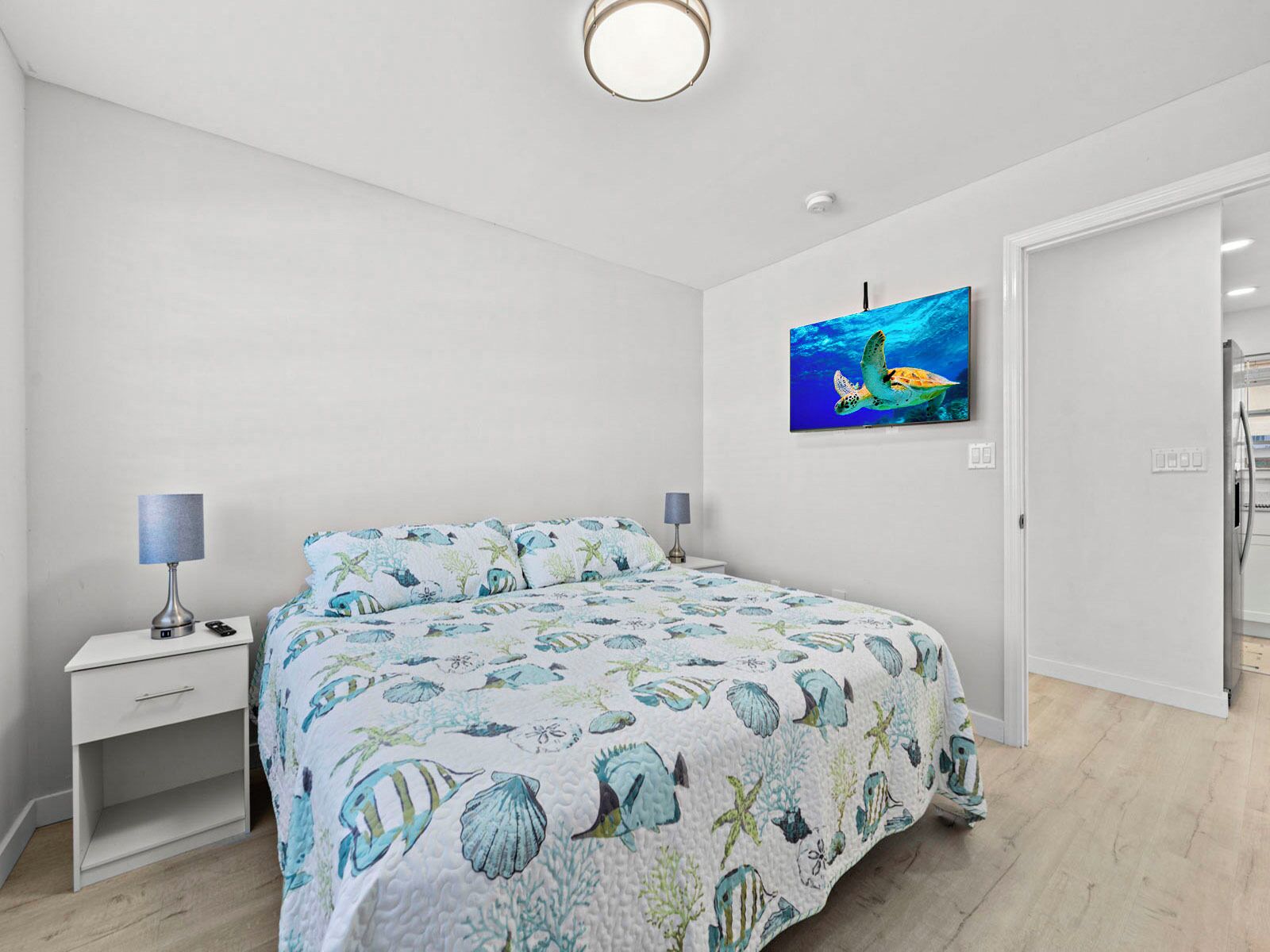 A bedroom with a bed, nightstands, a painting of a sea turtle, and a door leading to another room.