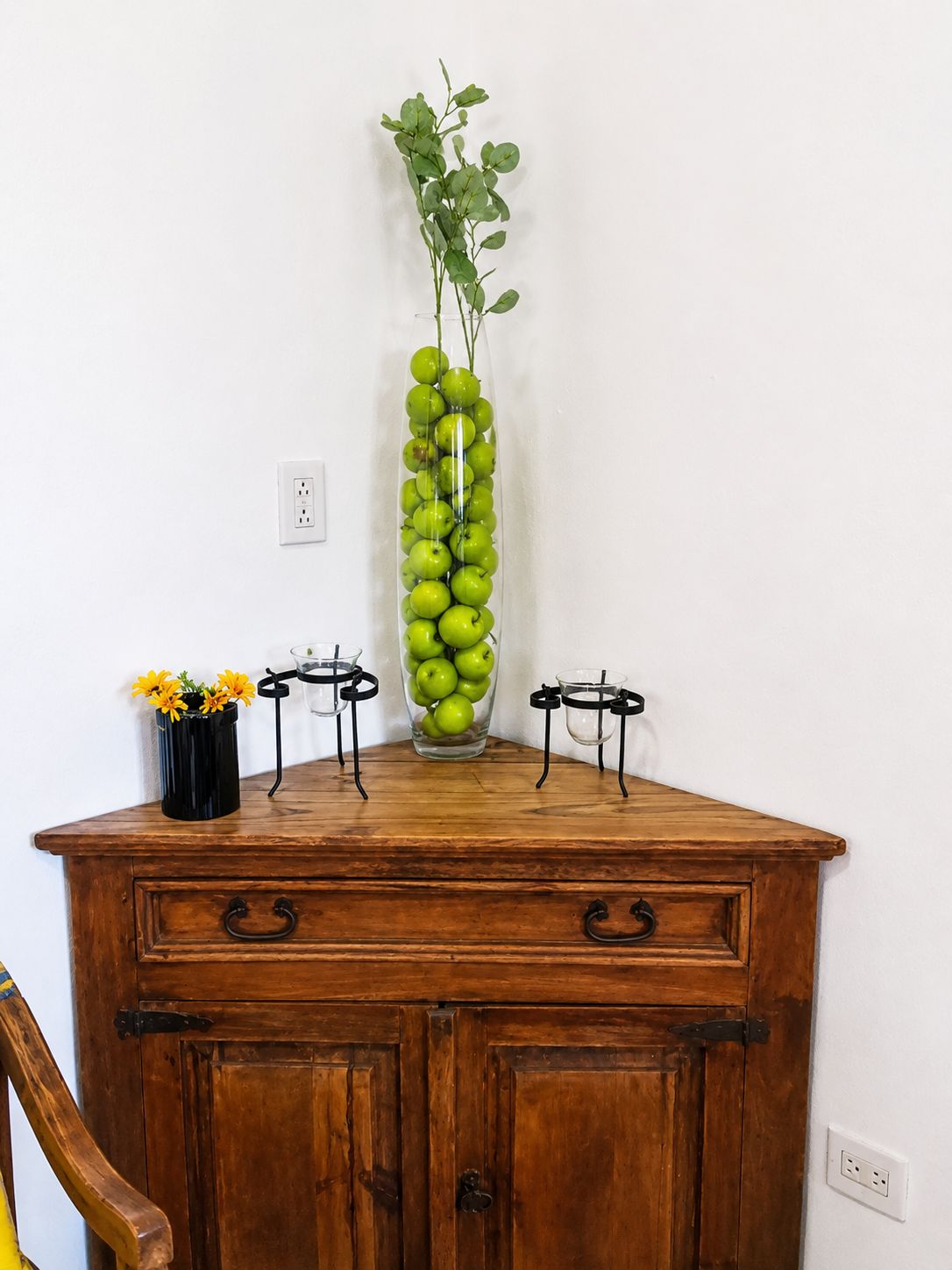 Un meuble en bois surmonté d’un vase contenant des pommes vertes et d’une plante en pot.