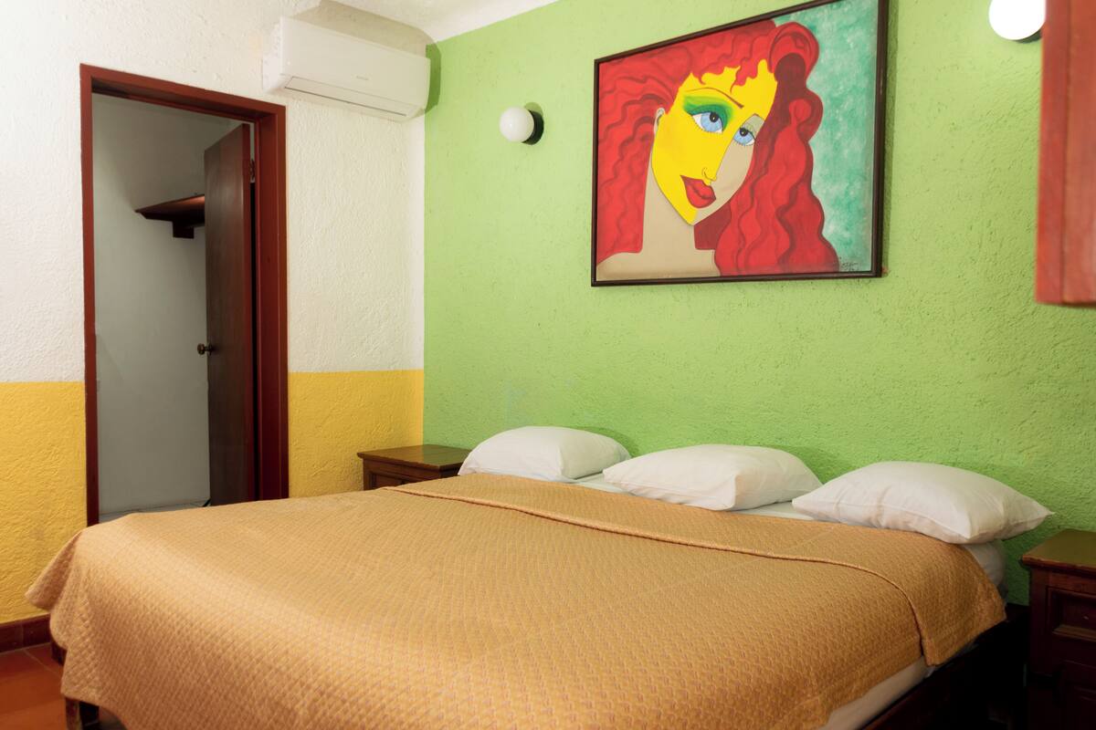 Une pièce avec un lit, un tableau au mur et une porte.