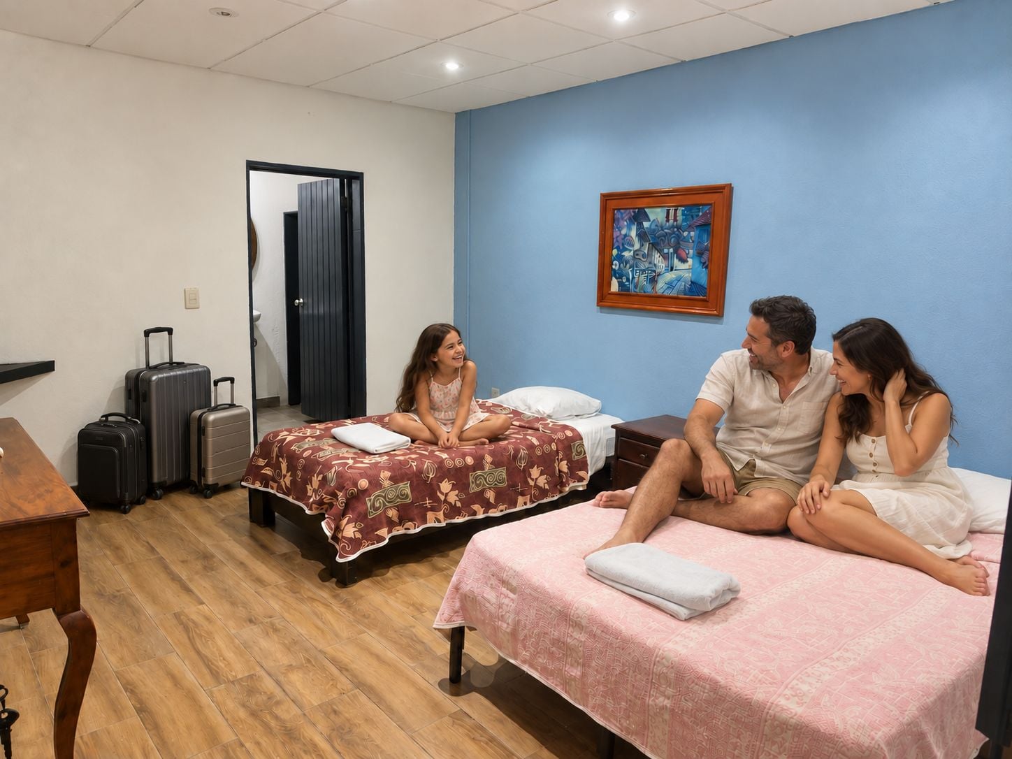 Une chambre avec deux lits, un bureau et une chaise. On y trouve des valises et un tableau accroché au mur.