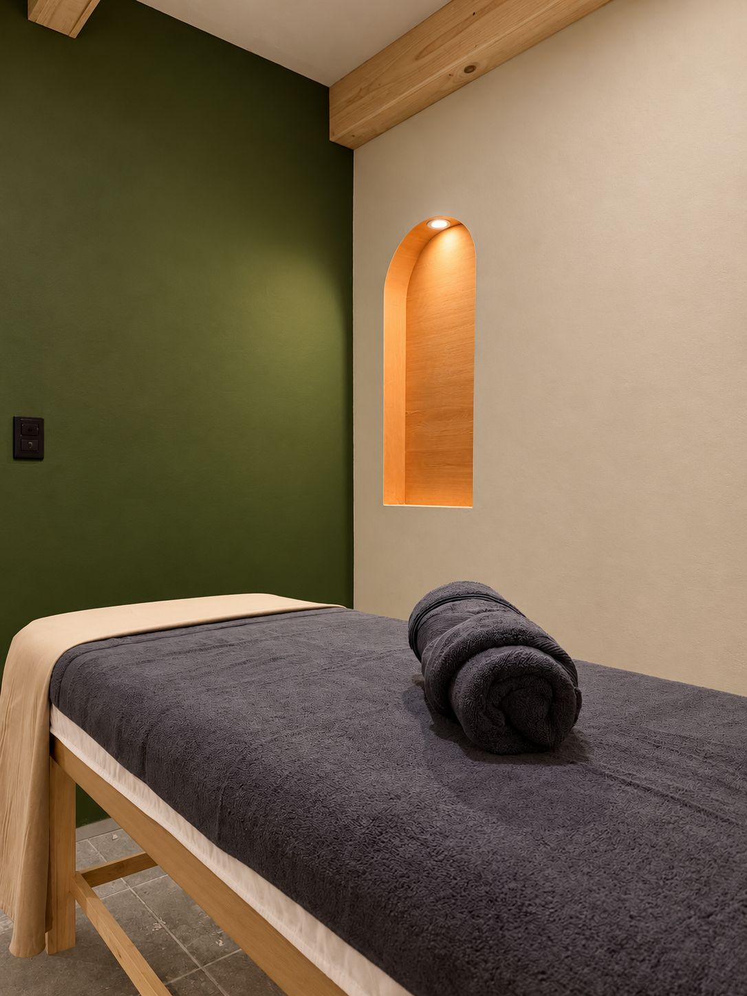 Una cama individual con una colcha texturizada oscura, una toalla enrollada y un cabecero de madera.