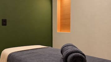Una cama individual con una colcha texturizada oscura, una toalla enrollada y un cabecero de madera.