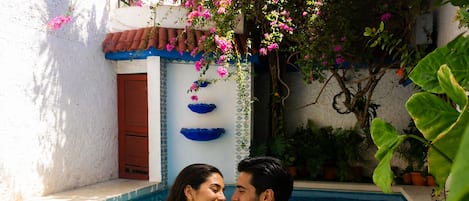 A couple in a swimming pool with a tiled wall and potted plants.