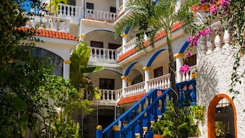 Zona de piscina con un edificio de dos plantas al fondo, con balcones y una escalera.