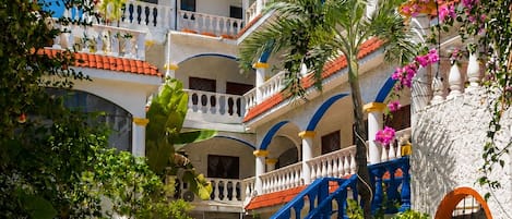 Zona de piscina con un edificio de dos plantas al fondo, con balcones y una escalera.