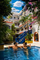 Zona de piscina con un edificio de dos plantas al fondo, con balcones y una escalera.