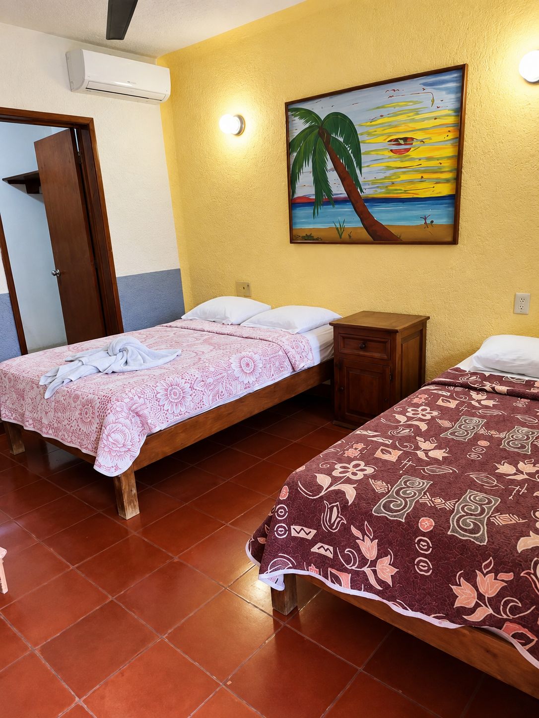 Een kamer met twee bedden, een schilderij van een strand en een airconditioning.