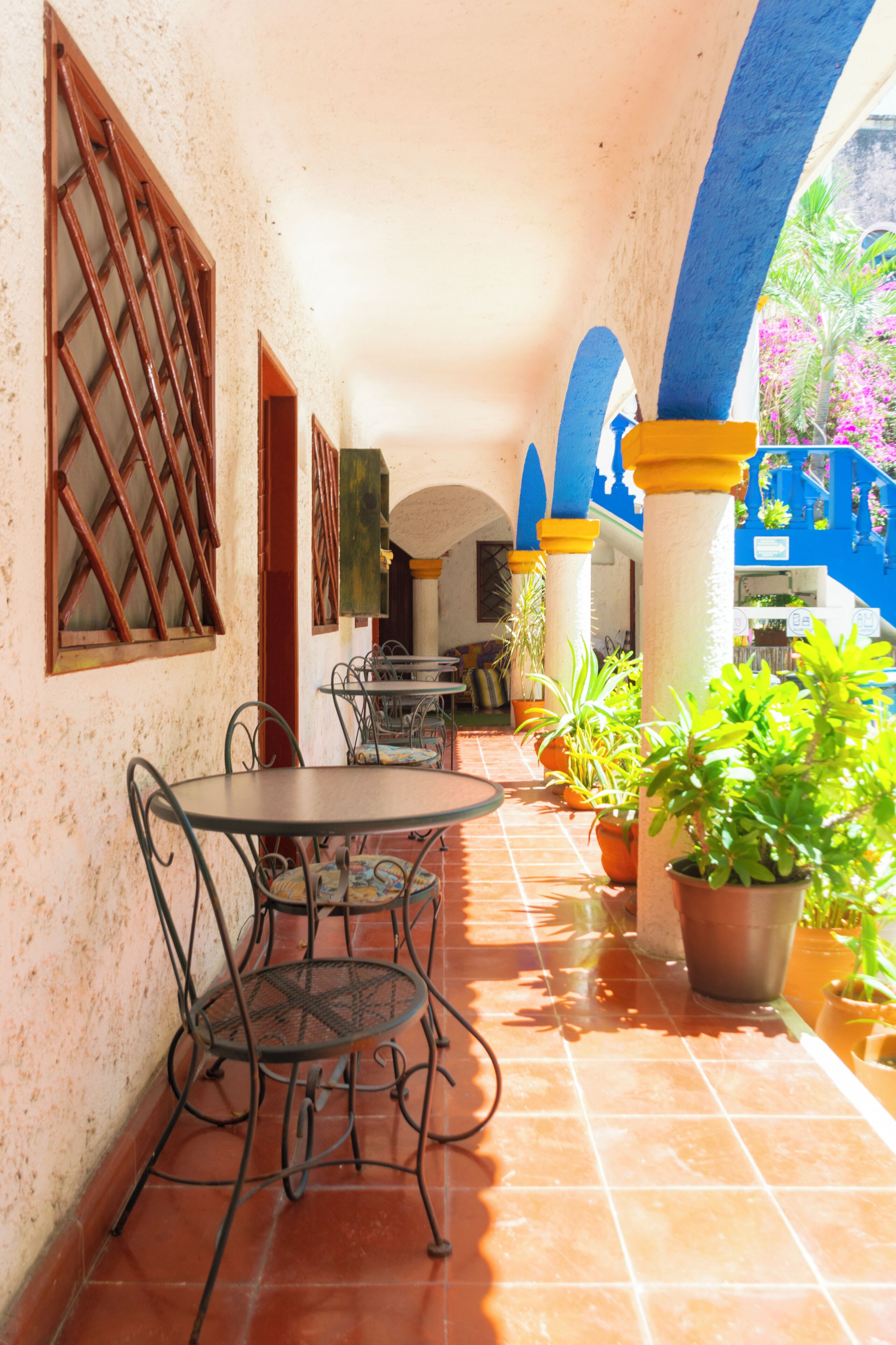 A covered patio with a round table and chairs, potted plants, and a blue and yellow architectural design.
