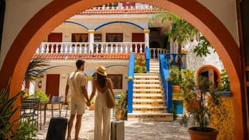 Une cour intérieure avec un escalier central, un couple se tenant la main et un homme avec une valise.