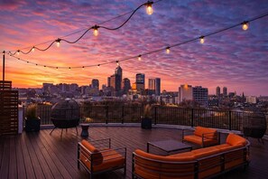 En takterrass med utomhusmöbler, utsikt över stadens skyline och ljusslingor.