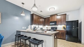 A modern kitchen with dark wooden cabinets, a central island with bar stools, stainless steel appliances, and pendant lighting. - Spacious Modern 2BR 2Bath | Free Parking | Near City Center (Indianapolis)