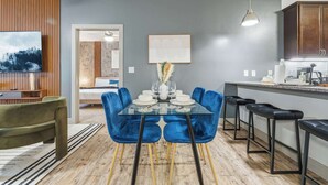 A modern kitchen with a dining area, featuring a glass table, blue chairs, and wooden accents. - Spacious Modern 2BR 2Bath | Free Parking | Near City Center (Indianapolis)