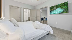Een slaapkamer met een bed, een plafondventilator, een schilderij van een rivier en een deur naar een badkamer.