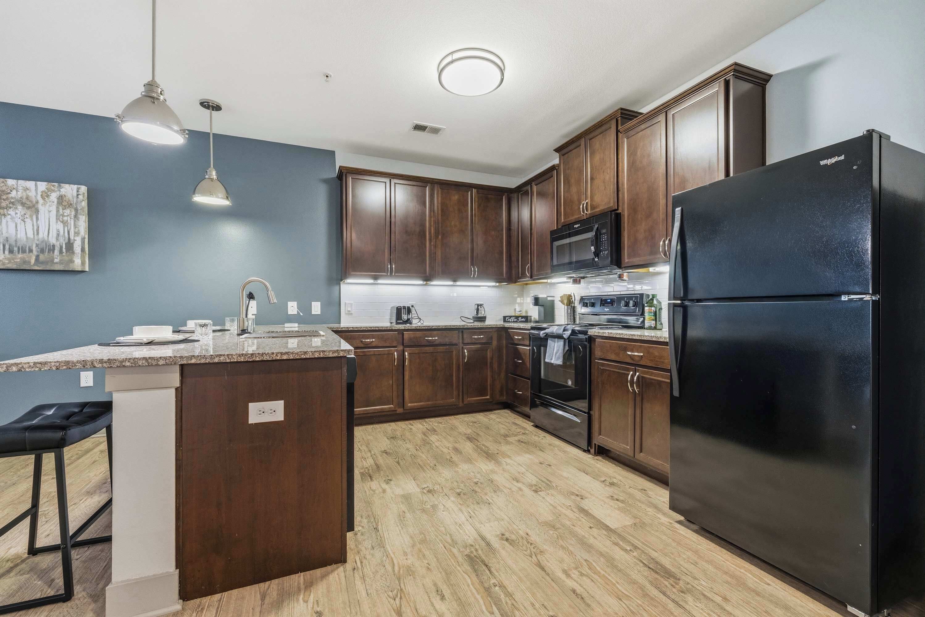A kitchen with wooden cabinets, a black refrigerator, a microwave, and a sink.