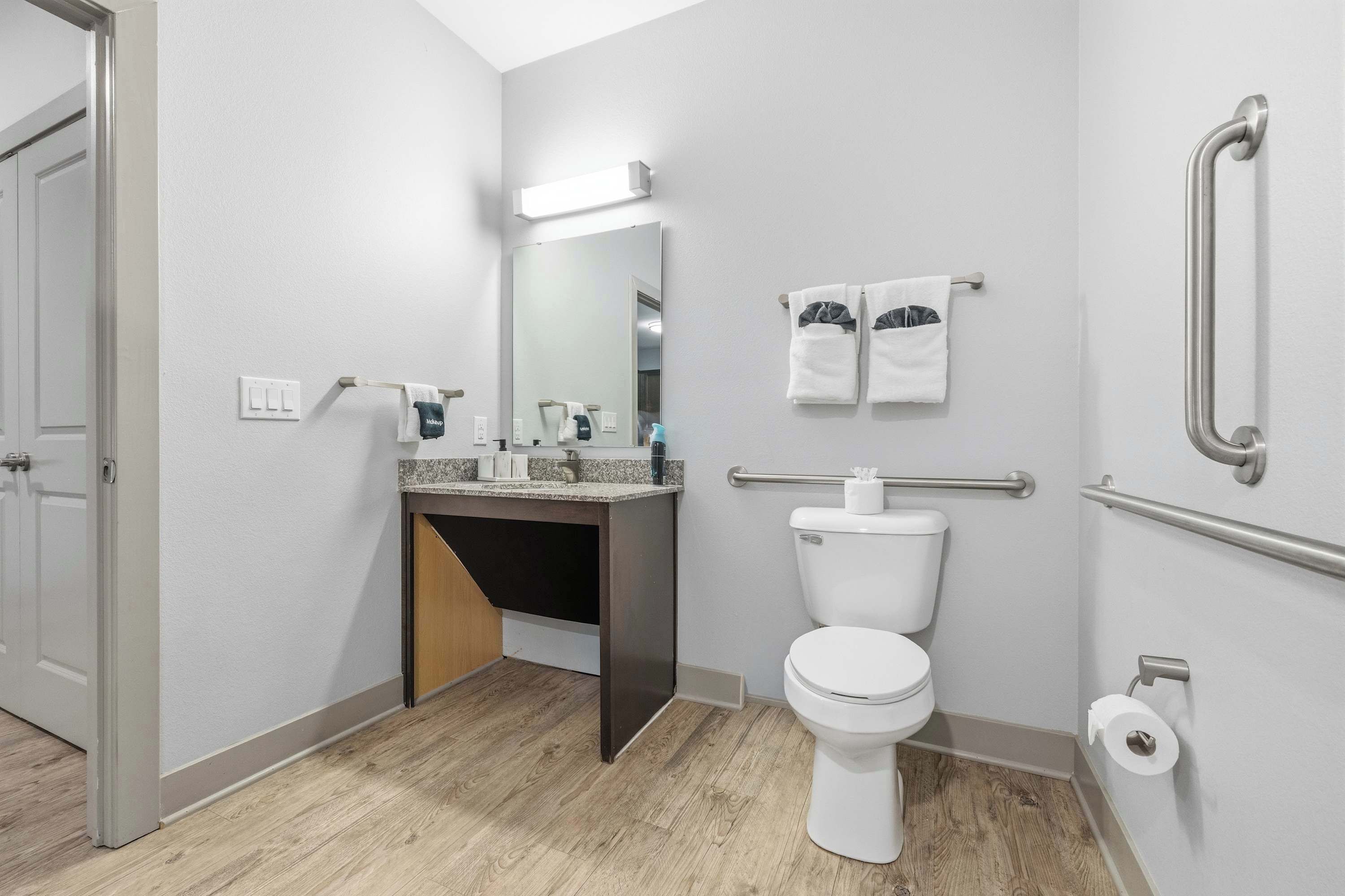 Un bagno moderno con toilette, lavandino, specchio, porta asciugamani e maniglie di sostegno.