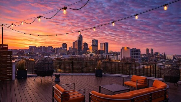 A rooftop terrace with outdoor seating, a city skyline view, and string lights. - Spacious Modern 2BR | Free Parking | Near City Center (Indianapolis)
