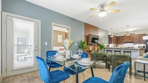 A modern dining area with a glass table, blue chairs, and a ceiling fan. - Spacious Modern 2BR | Free Parking | Near City Center (Indianapolis)