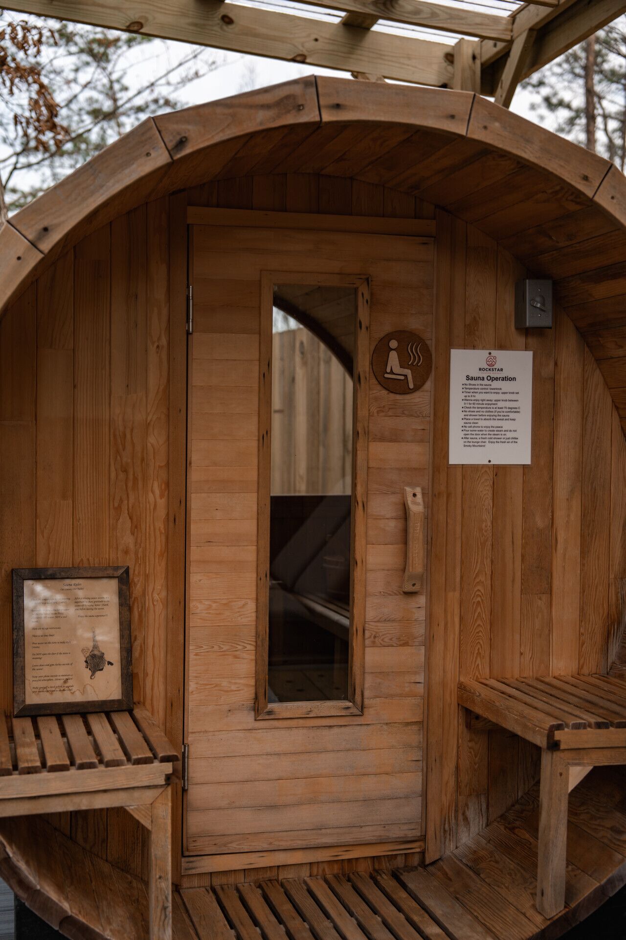 Eine Holzhütte als Sauna mit Tür, Sitzbank und einem Schild, das die Saunabetreibung erklärt.