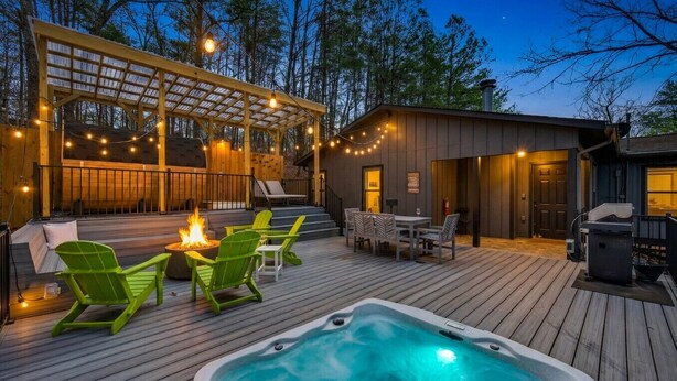 Eine Holzterrasse mit Whirlpool, grünen Sesseln und einer überdachten Sitzecke mit Lichterketten.