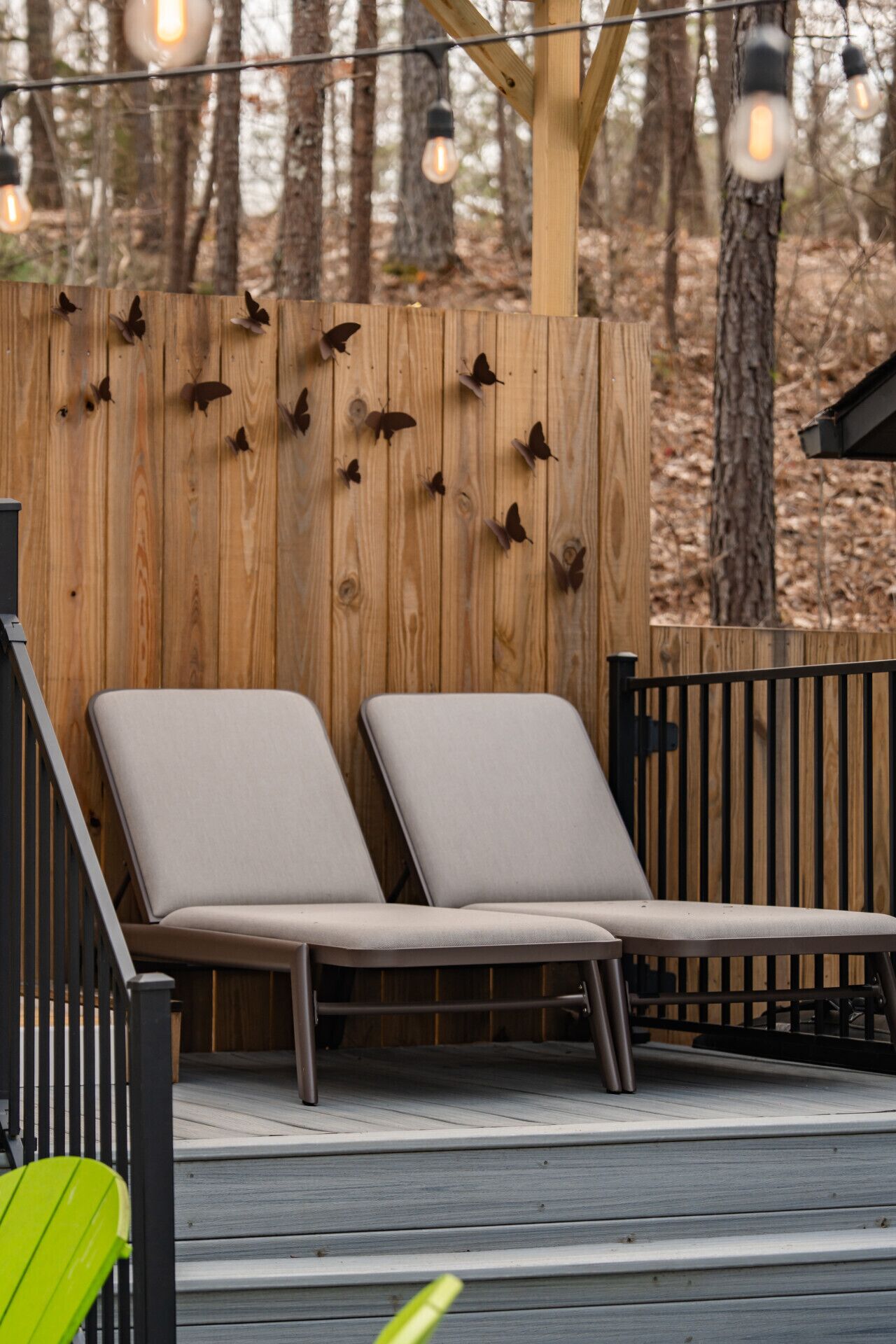 A wooden deck with two lounge chairs and a wooden fence with butterfly decorations.