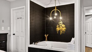 Ein modernes Badezimmer mit Schwarz-Weiß-Farbgebung, einer freistehenden Badewanne und einer einzigartigen, goldfarbenen Leuchte in Form eines Baumes.