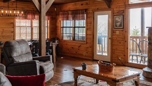 L’intérieur chaleureux d’un chalet, avec des murs et un plafond en bois, un coin repas comprenant une table et des chaises, et une grande fenêtre donnant sur le paysage extérieur.