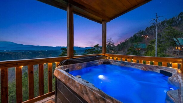 Un bain à remous sur une terrasse en bois, offrant une vue sur un paysage montagneux au crépuscule.
