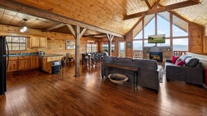 Un intérieur de chalet en bois spacieux, comprenant un coin repas, une cuisine et un salon avec une cheminée.