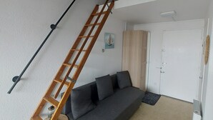 Une pièce de style loft avec une échelle en bois, un canapé gris et une porte blanche.