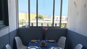 Un coin repas avec une table dressée pour quatre personnes, de grandes fenêtres et une vue sur les bâtiments.