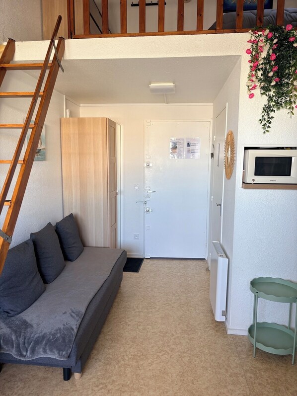 A bedroom with a bed, a ladder, a door, a wall-mounted TV, and a small table.