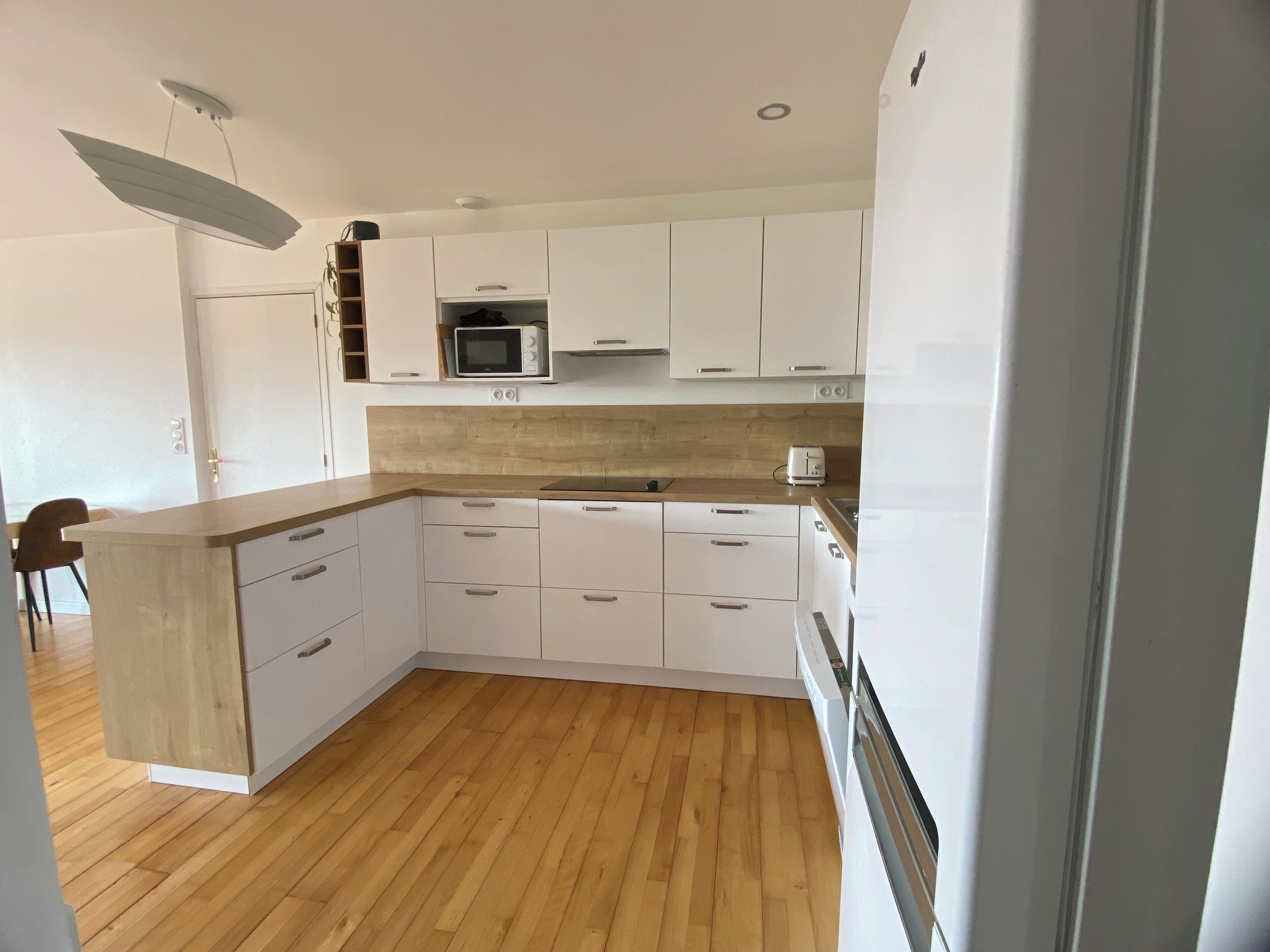 Une cuisine moderne avec des meubles blancs, un plan de travail en bois, un four à micro-ondes et un grille-pain.