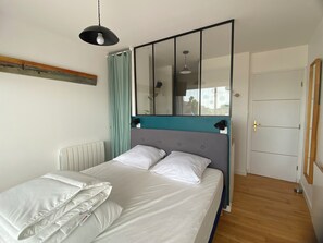 Ein Bett mit weißer Bettwäsche, eine Wand in Türkis, ein großer Spiegel und eine Hängeleuchte.