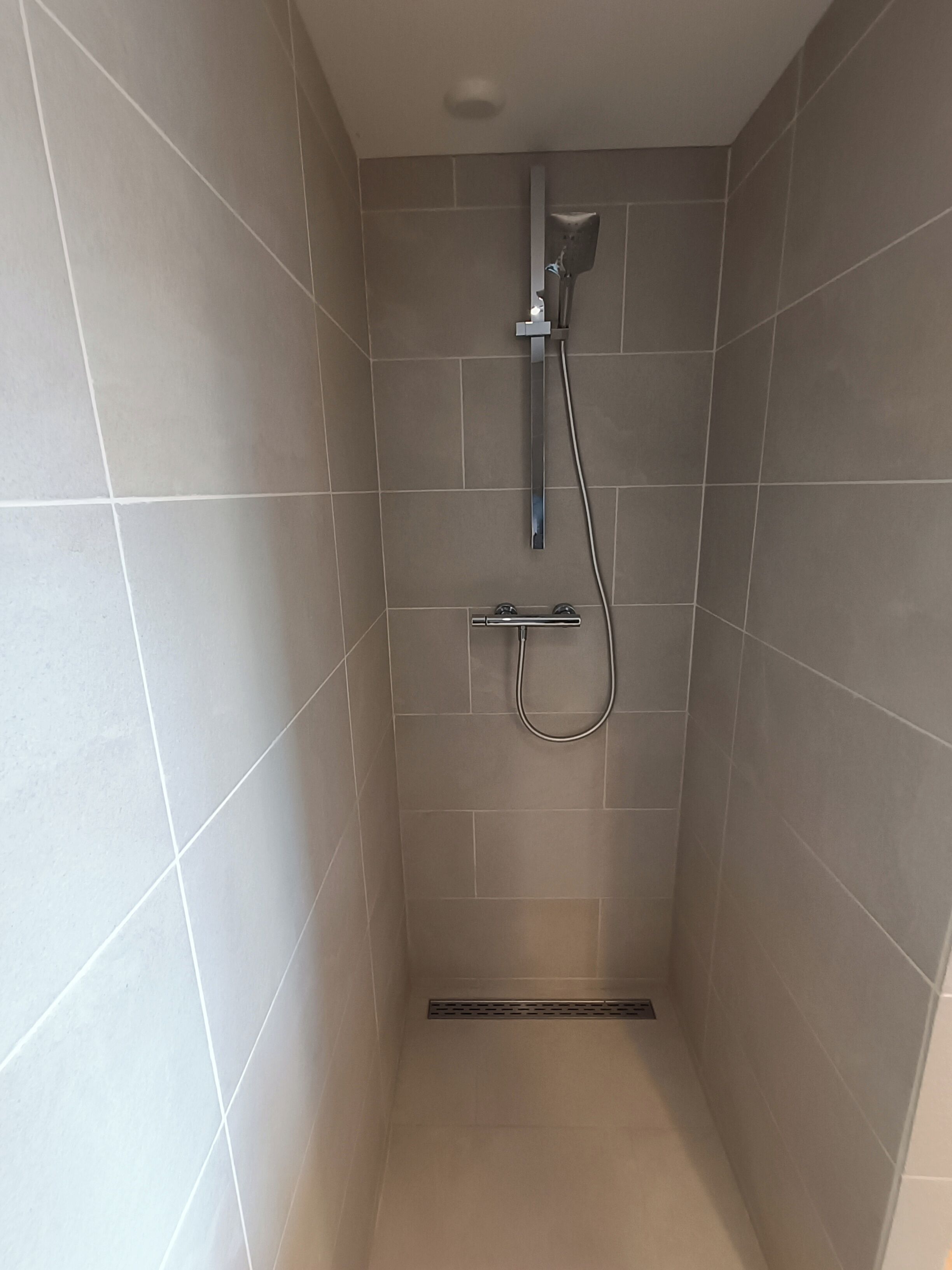 A small, tiled shower stall with a handheld showerhead and a wall-mounted faucet.