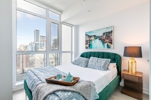 A bedroom with a large window, a bed with green bedding, a city view, a painting on the wall, and a bedside lamp. - Noyaa Toronto - The Entertainment District (Toronto)