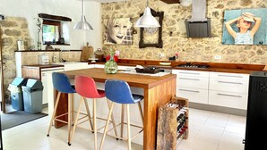 A kitchen with a wooden island, bar stools, a wine rack, and a stone wall. - Luxueuse maison de campagne isolée, nichée dans la forêt au milieu des oiseaux. (Lesparrou)