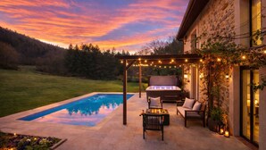 A pool with a pergola and outdoor seating, a stone building, and a sunset view. - Luxueuse maison de campagne isolée, nichée dans la forêt au milieu des oiseaux. (Lesparrou)