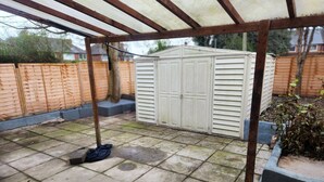 A covered patio area with a metal roof, a storage shed, and a garden bed with plants. - Come and Enjoy My Peaceful Home, Your Comfort Zone (Manchester)