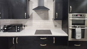 A kitchen with black cabinets, a stainless steel range hood, a built-in oven, and a microwave. - Come and Enjoy My Peaceful Home, Your Comfort Zone (Manchester)