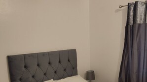 A bed with a tufted headboard, a bedside lamp, and a dark curtain. - Come and Enjoy My Peaceful Home, Your Comfort Zone (Manchester)