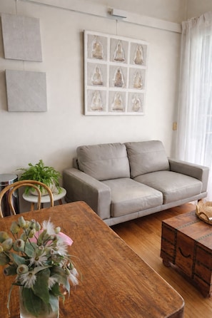A living room with a grey sofa, a wooden dining table, and a vase with flowers.