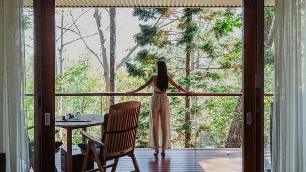 A woman standing on a wooden deck with a railing, overlooking a forested area. - Taman Sari Luxury Private Pavilions (Mapleton)